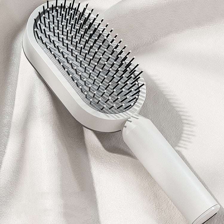 Self-cleaning hair brush with gray cushioned pad and dense black pins, white handle