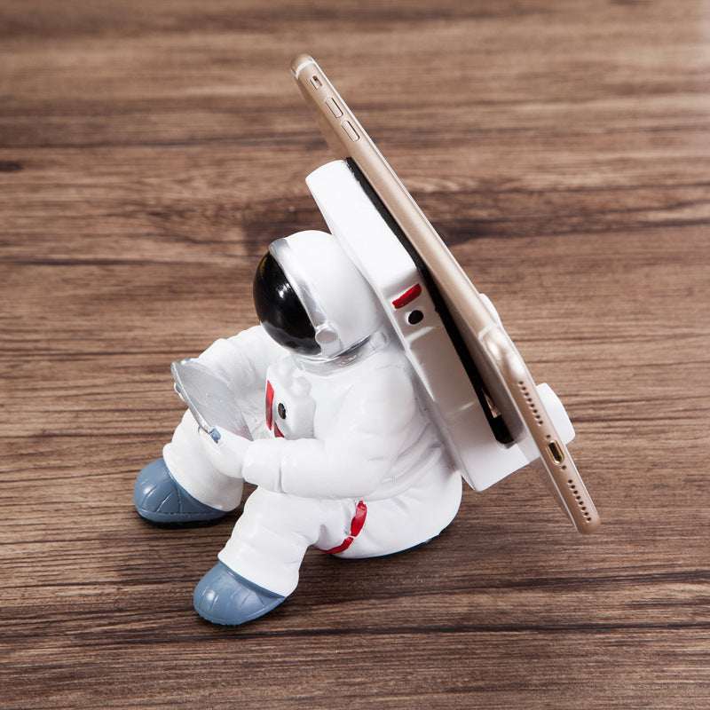 Astronaut phone stand with seated white spaceman holding a smartphone
