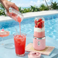 Portable electric blender juicer with pink base and clear jar filled with strawberry smoothie