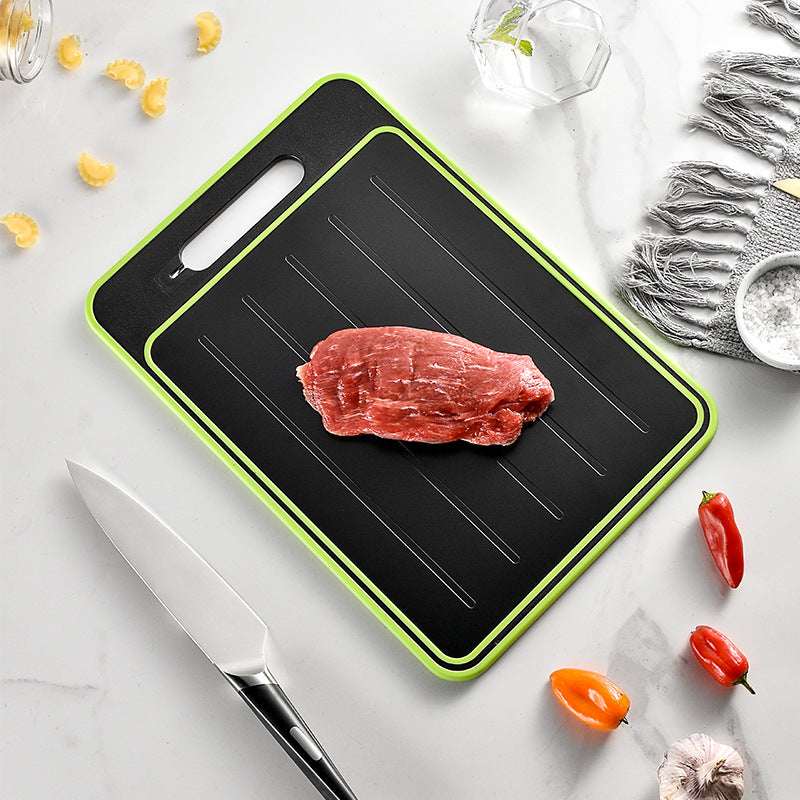 Square grey cutting board with green border and black surface, knife and meat portion visible