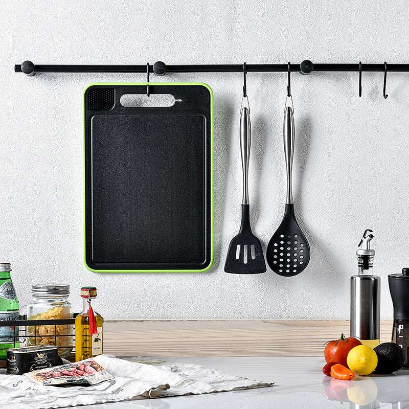 Square kitchen cutting board with black surface and green border, with hanging utensil hooks